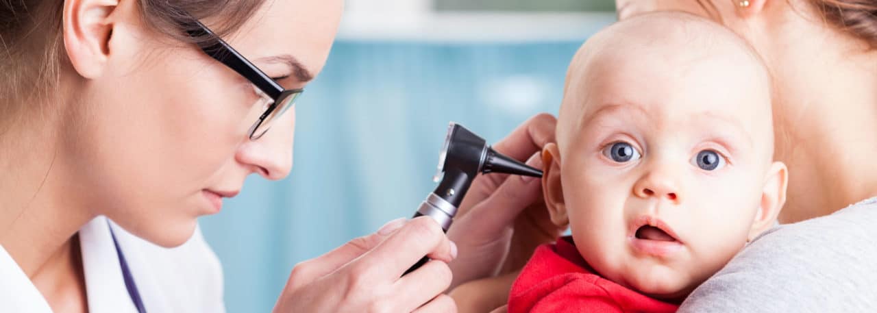 A baby being examined by an audiologist with an otoscope