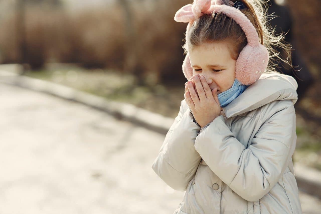 Little girl covering her nose while outside.