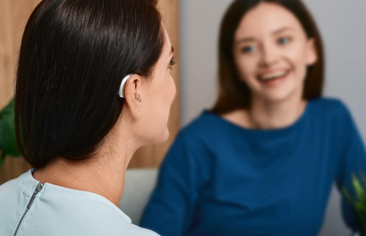 Young woman with a hearing aid talking with her friend at home.
