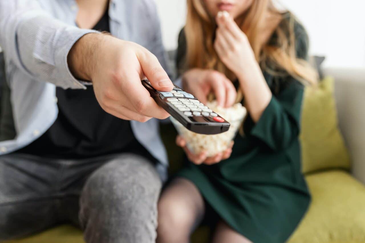 Close up of a couple watching TV with the man pointing the remote.