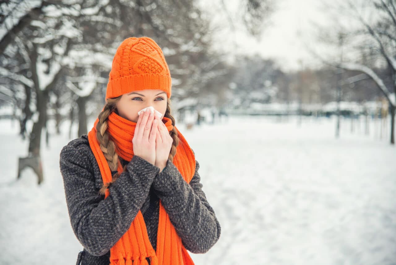 Young woman outside in the park in winter blowing her nose.