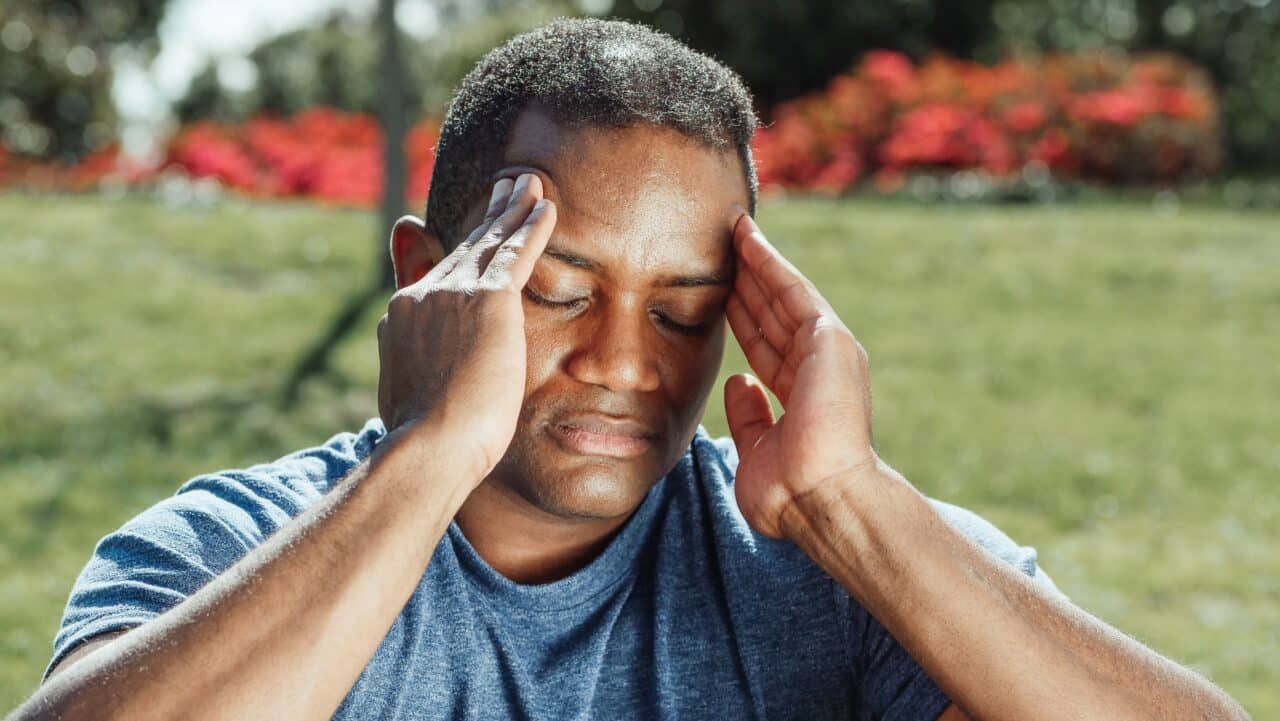 Man sitting outside suffering with a headache.