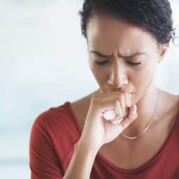 Young woman coughing in an office building.