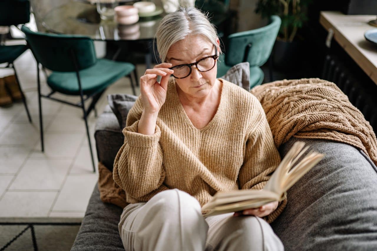 Senior woman with glasses reading on her couch.