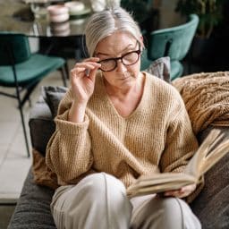 Senior woman with glasses reading on her couch.