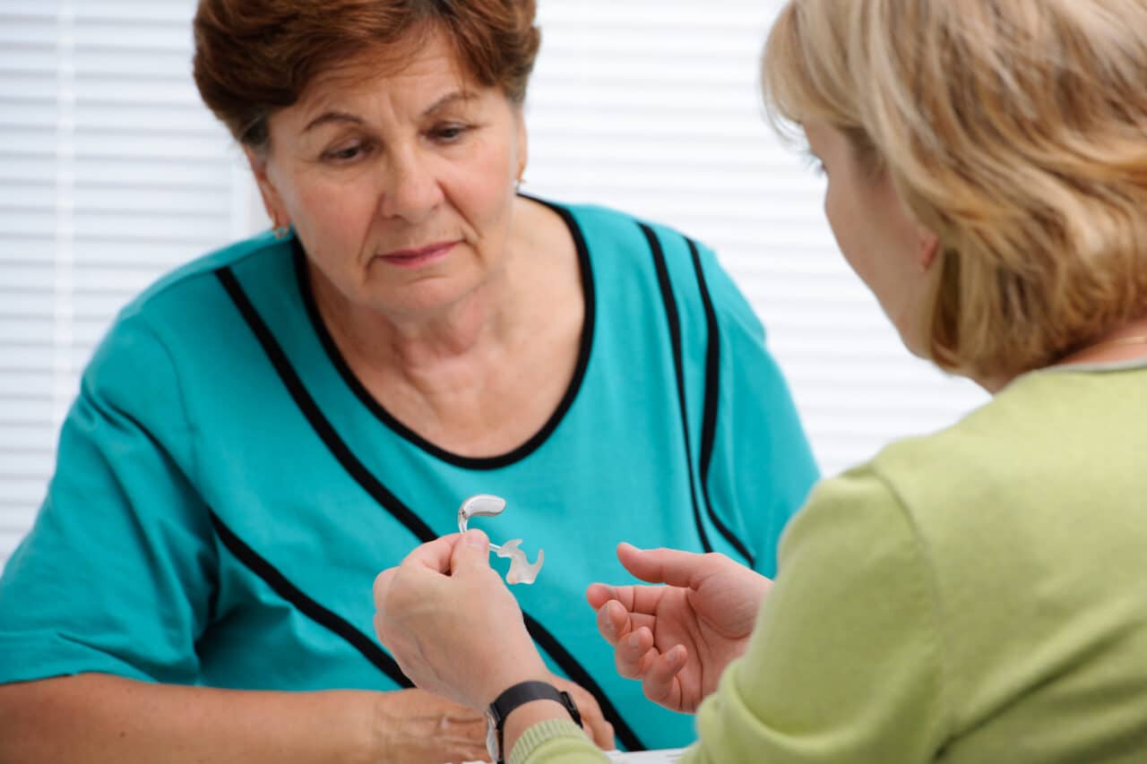 Audiologist going over how to use a hearing aid with a senior female patient.