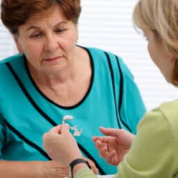 Audiologist going over how to use a hearing aid with a senior female patient.