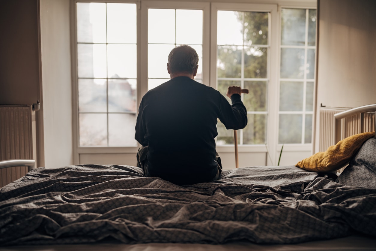 Sad man sitting on a bed looking out towards the window.