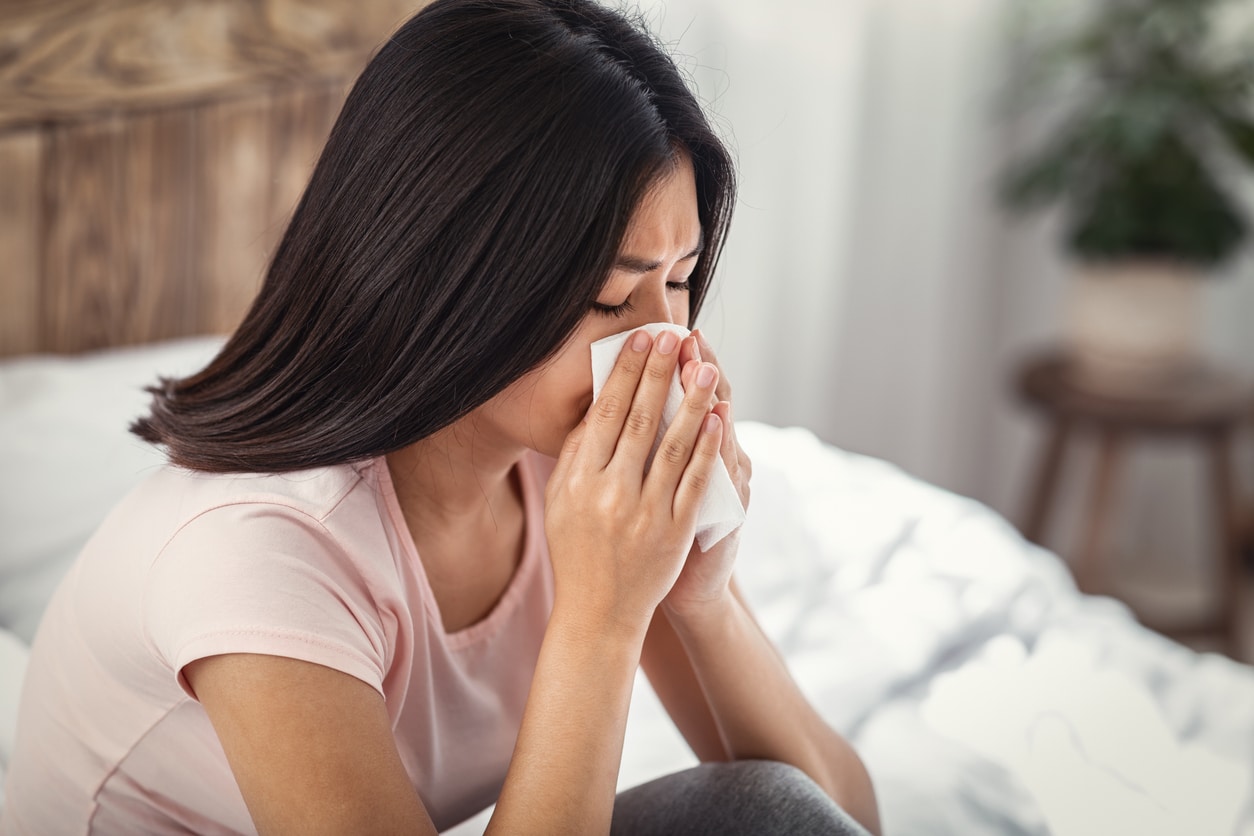 Young woman blowing her nose into a tissue at home.