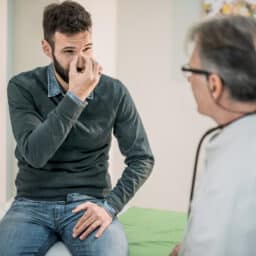 Man showing a doctor where on the bridge of his nose he's experiencing symptoms