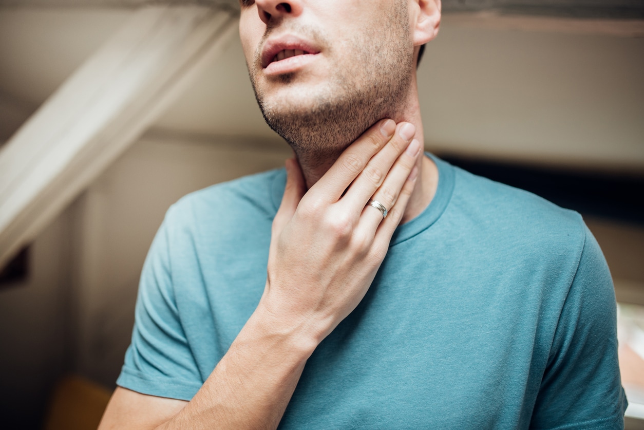 Young man touching his sore throat.