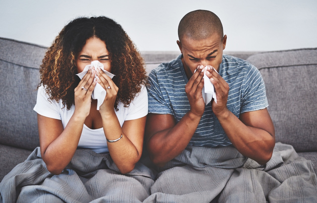 Couple with allergies sneezing on the couch.