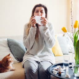 Woman sitting next to a cat in her home about to sneeze into a tissue