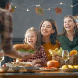 Senior woman adding a turkey to the Thanksgiving table surrounded by her happy family