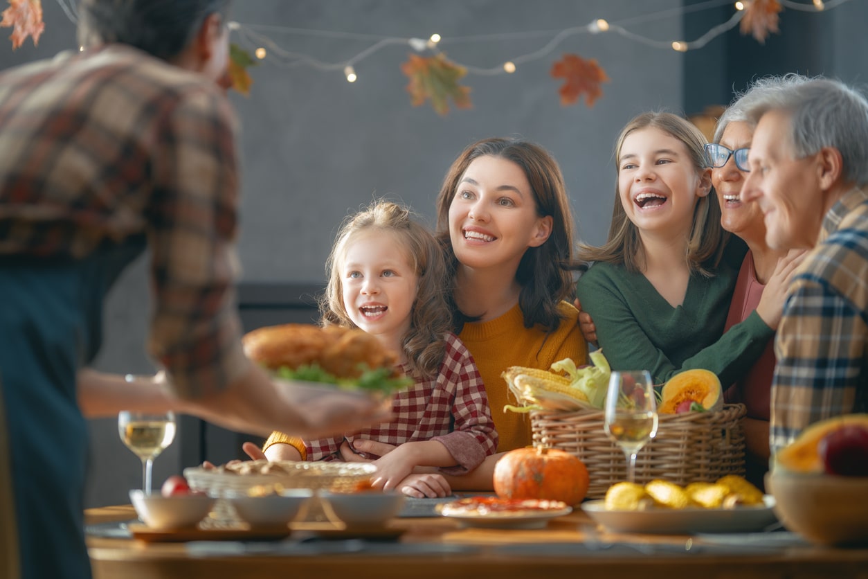 Senior woman adding a turkey to the Thanksgiving table surrounded by her happy family.