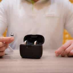 audiologist in his office with one hearing aid in his hand and two hearing aids in their case